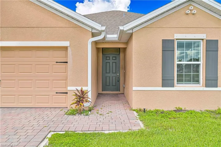 Entrance to property with stucco siding, a garage, roof with shingles, and a lawn