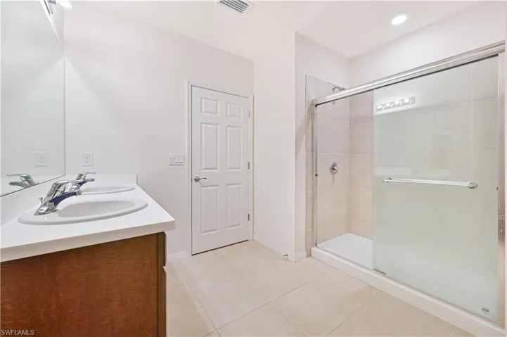 Bathroom featuring a stall shower, light tile patterned flooring, double vanity, and recessed lighting