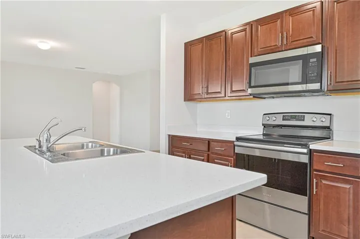 Kitchen with appliances with stainless steel finishes, light stone countertops, arched walkways, light tile patterned floors, and brown cabinets