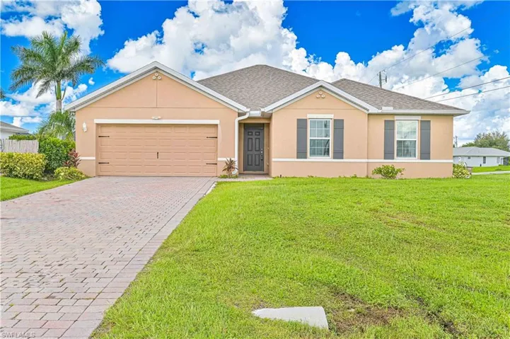 Ranch-style home with stucco siding, an attached garage, a front lawn, decorative driveway, and roof with shingles