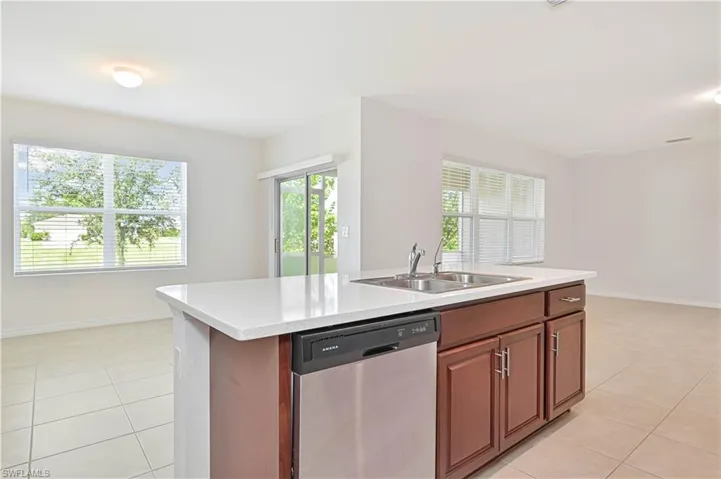 Kitchen with dishwasher, a center island with sink, light tile patterned floors, and brown cabinets