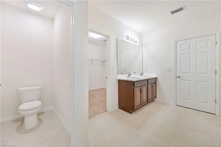 Bathroom with double vanity, light tile patterned floors, and a walk in closet