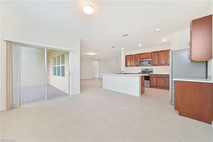 Kitchen with light countertops, stainless steel appliances, brown cabinets, recessed lighting, and an island with sink