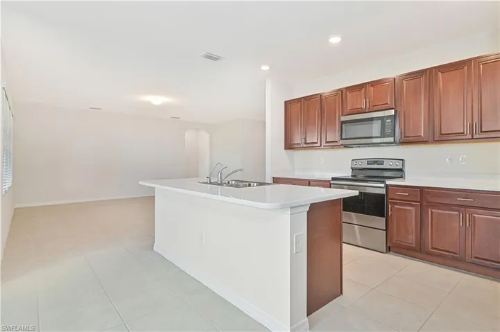 Kitchen featuring stainless steel appliances, arched walkways, a kitchen island with sink, light tile patterned flooring, and recessed lighting