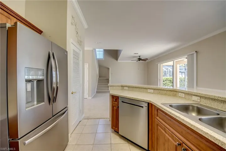 Kitchen featuring stainless steel appliances, wood finish cabinetry, ornamental molding, light stone counters, and light tile patterned floors