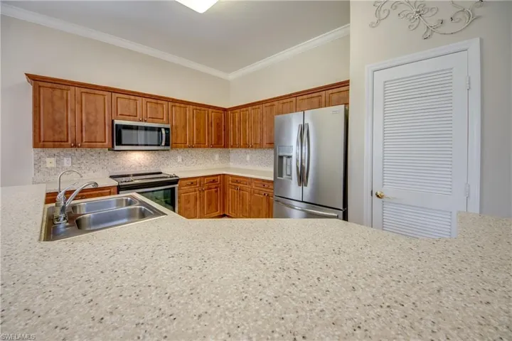 Kitchen with stainless steel appliances, backsplash, wood finish cabinets, ornamental molding, and light stone counters
