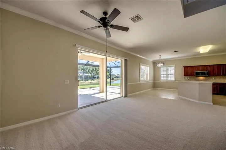 Unfurnished living room with crown molding, light colored carpet, ceiling fan, a sunroom, and hanging lights