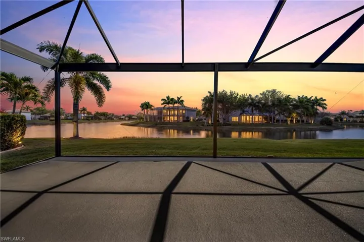 Patio terrace at dusk featuring a water view, a yard, and glass enclosure