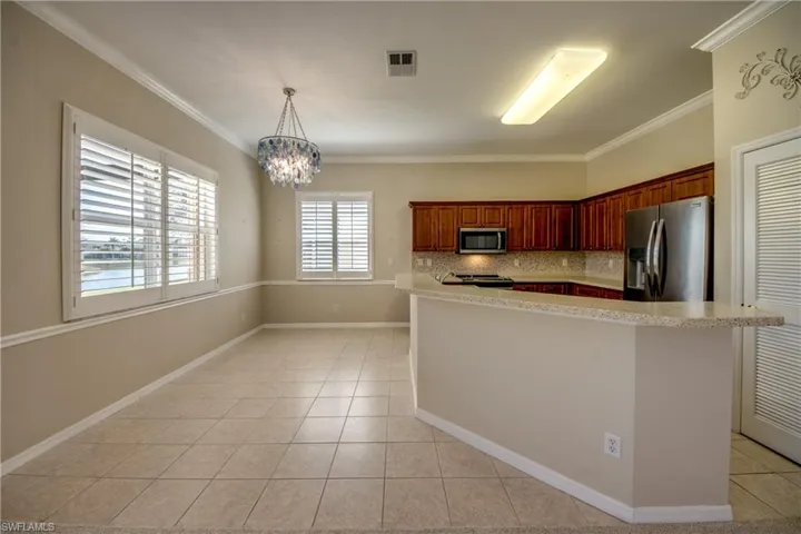 Kitchen with stainless steel appliances, suspended lighting, tasteful backsplash, ornamental molding, and light tile patterned floors