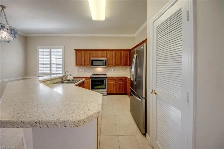 Kitchen with stainless steel appliances, ornamental molding, backsplash, a spacious island, and light tile patterned flooring