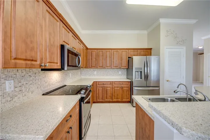 Kitchen with stainless steel appliances, backsplash, wood finish cabinetry, ornamental molding, and light tile patterned floors