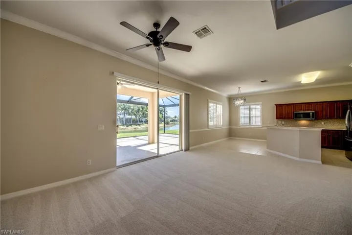 Unfurnished living room featuring a ceiling fan, ornamental molding, light carpet, plenty of natural light, and a chandelier