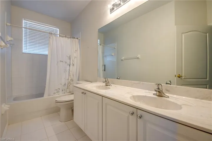 Bathroom featuring double vanity, shower / bath combo, and light tile patterned flooring