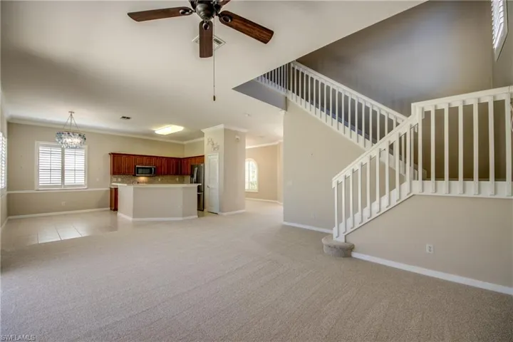 Unfurnished living room with crown molding, ceiling fan, light colored carpet, healthy amount of natural light, and suspended lighting