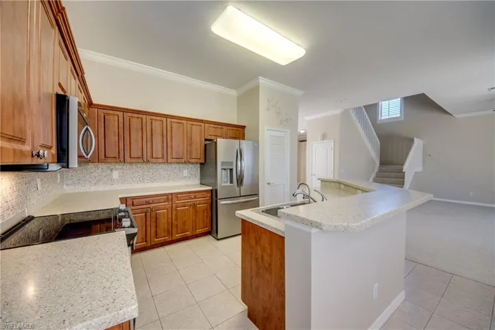 Kitchen with wood finish cabinetry, crown molding, stainless steel appliances, a center island with sink, and light tile patterned floors
