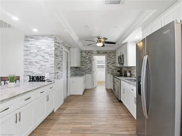 Kitchen featuring appliances with stainless steel finishes, a raised ceiling, white cabinetry, light stone counters, and crown molding