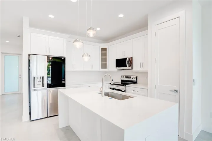 Kitchen with stainless steel appliances, white cabinetry, light stone countertops, and a kitchen island with sink
