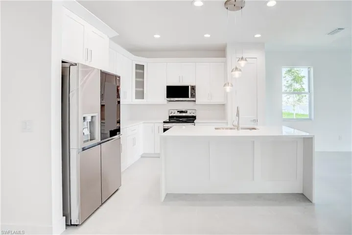 Kitchen featuring stainless steel appliances, white cabinets, a kitchen island with sink, light stone counters, and pendant lighting
