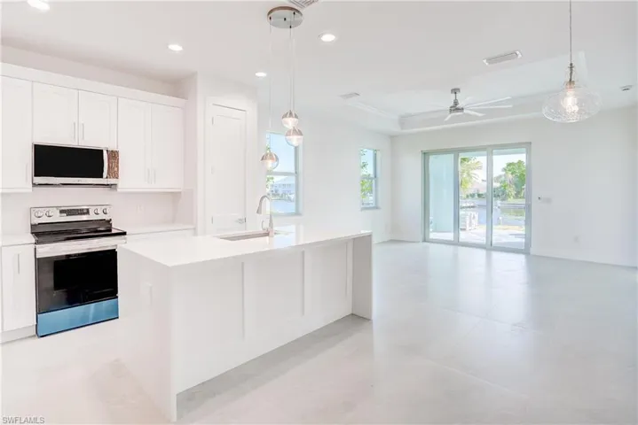 Kitchen with stainless steel electric stove, an island with sink, white cabinets, open floor plan, and light stone counters