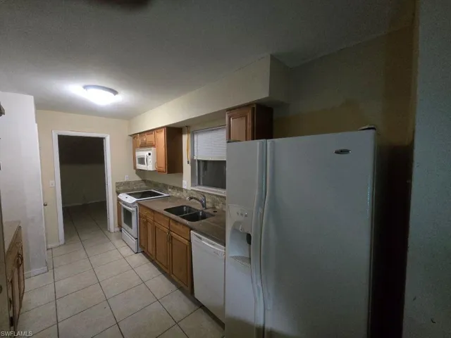 Kitchen with white appliances, wood finish cabinets, and light tile patterned floors