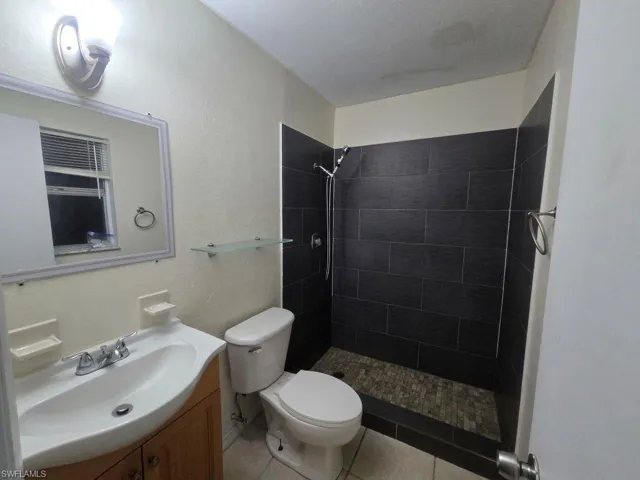 Bathroom featuring a shower stall, vanity, light tile patterned floors, and a textured wall
