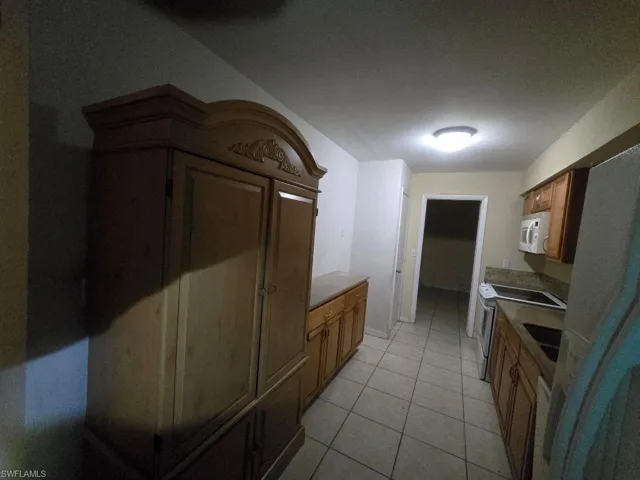Kitchen featuring white appliances, light tile patterned flooring, dark countertops, and wood finish cabinets