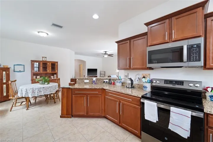 Kitchen with appliances with stainless steel finishes, arched walkways, brown cabinetry, light stone counters, and light tile patterned floors