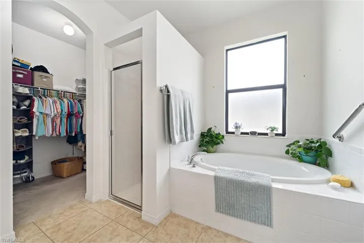 Full bathroom with a stall shower, a bath, a spacious closet, and light tile patterned flooring