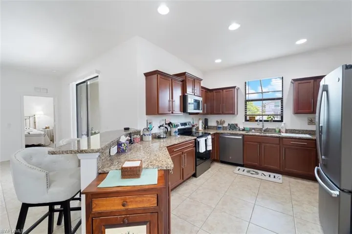 Kitchen with stainless steel appliances, a peninsula, light stone counters, a breakfast bar area, and light tile patterned floors