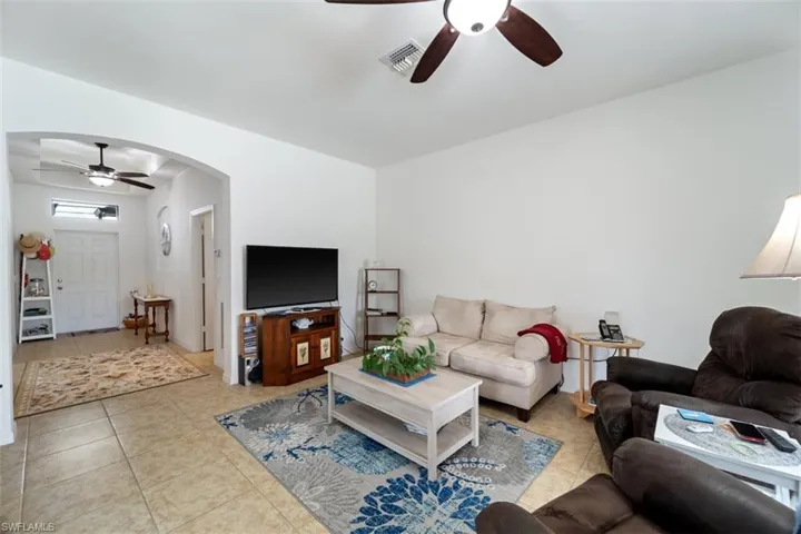 Living area with ceiling fan, light tile patterned floors, and arched walkways