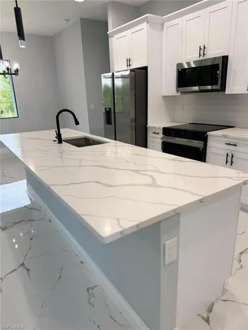 Kitchen with stainless steel appliances, a sink, marble look tiles, and white cabinets