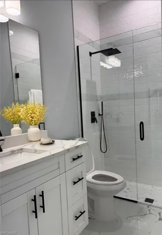 Bathroom featuring marble look tiles, a shower stall, vanity, and toilet