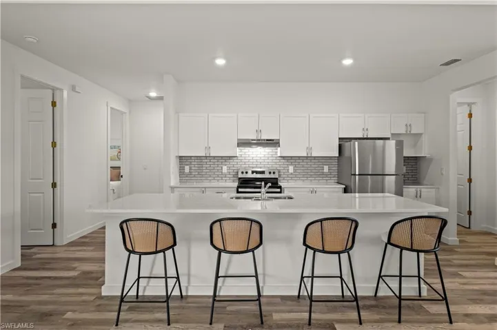 Kitchen featuring stainless steel appliances, hardwood / wood-style floors, and an island with sink