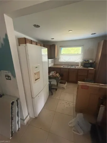 Kitchen with fridge, brown cabinets, light tile patterned flooring, and a sink