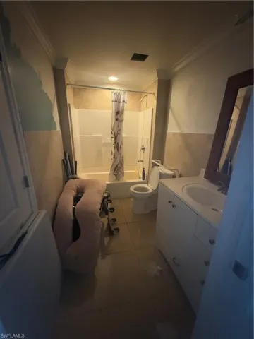 Bathroom featuring tile patterned flooring, crown molding, toilet, vanity, and shower / bathtub combination with curtain