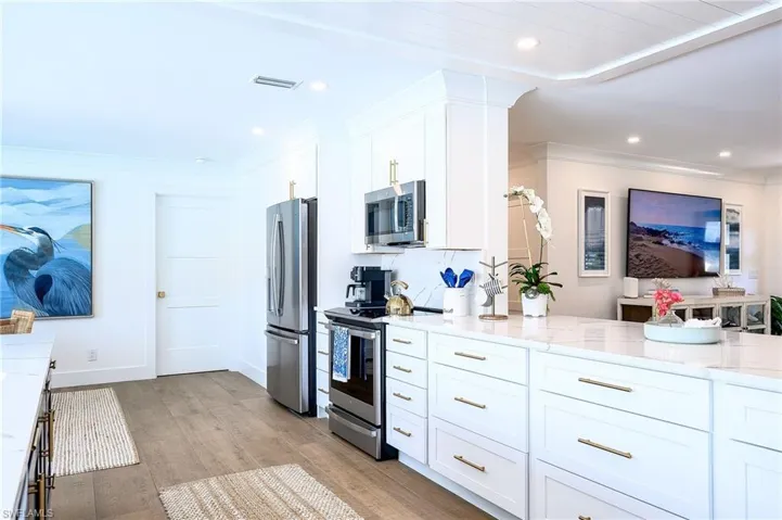 Kitchen featuring light stone counters, white cabinets, tasteful backsplash, stainless steel appliances, and light hardwood / wood-style floors