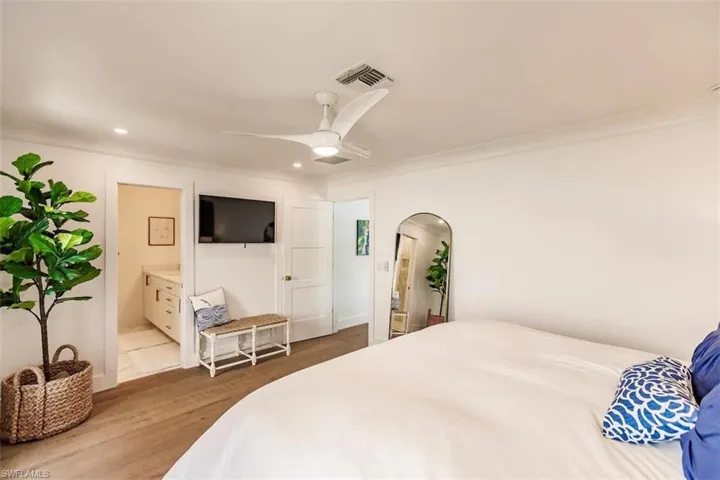 Bedroom featuring ceiling fan, light wood-type flooring, ensuite bath, and crown molding