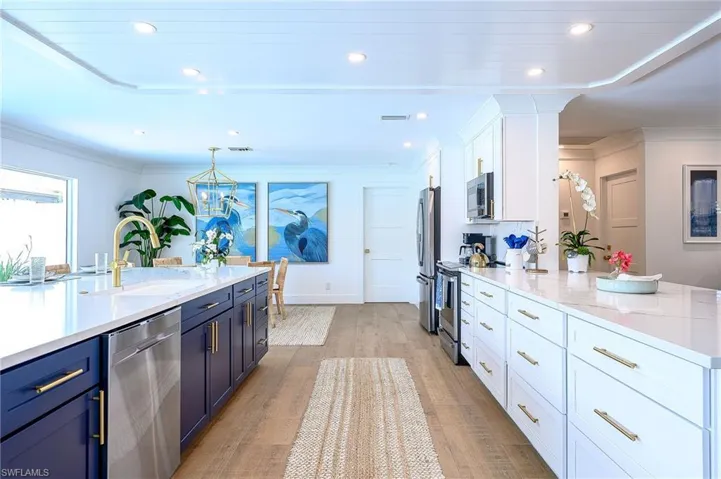 Kitchen with pendant lighting, light hardwood / wood-style floors, sink, white cabinets, and stainless steel appliances