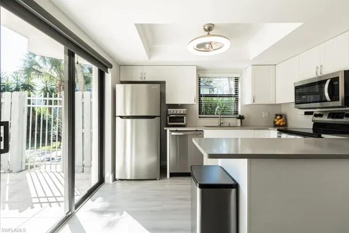 Kitchen with sink, stainless steel appliances, a raised ceiling, pendant lighting, and white cabinets