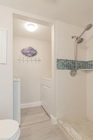 Bathroom with a tile shower, toilet, and washer / dryer
