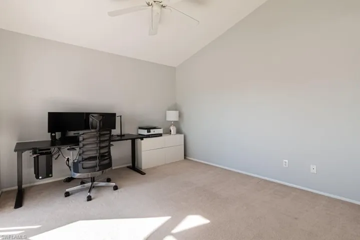 Carpeted office space with ceiling fan and vaulted ceiling