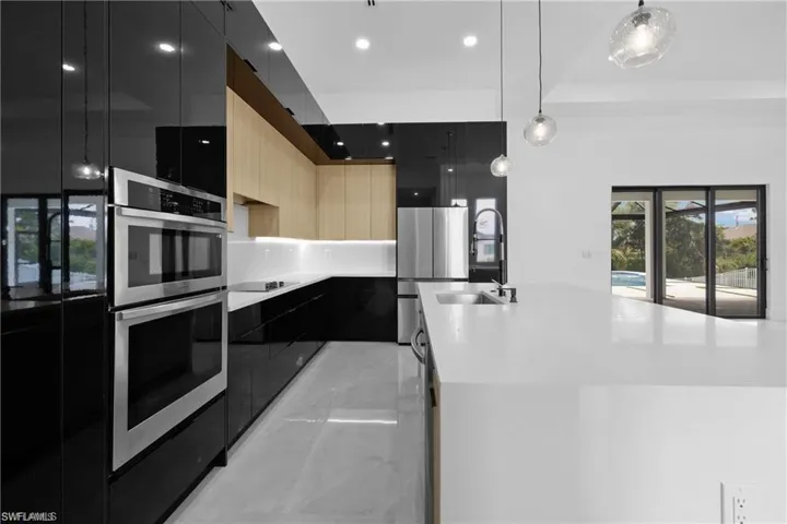 Kitchen with a center island with sink, appliances with stainless steel finishes, pendant lighting, sink, and light brown cabinets