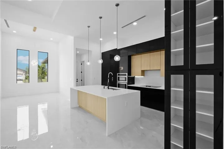 Kitchen with decorative light fixtures, sink, black electric stovetop, and a center island with sink