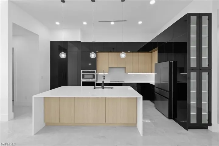 Kitchen with a large island with sink, light brown cabinets, black appliances, and decorative light fixtures