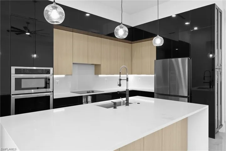 Kitchen with an island with sink, light brown cabinetry, pendant lighting, and appliances with stainless steel finishes