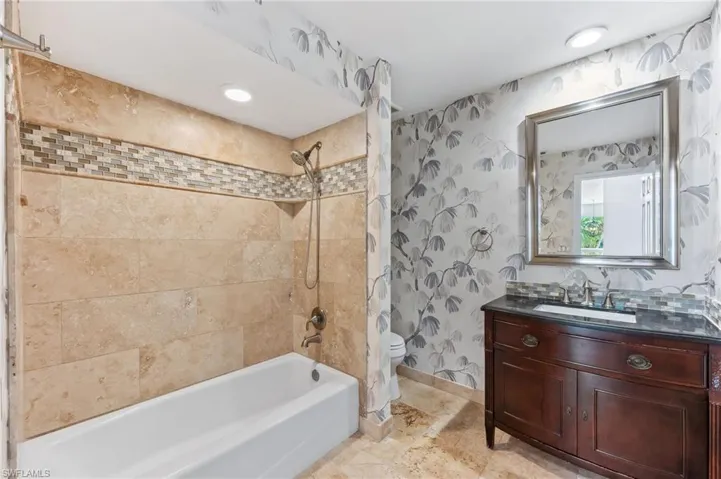 Full bath featuring wallpapered walls, baseboards, washtub / shower combination, toilet, and vanity