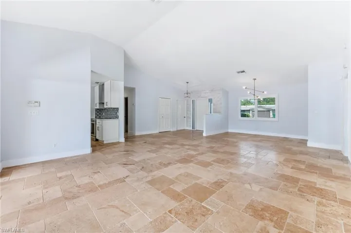 Unfurnished living room with visible vents, baseboards, stone tile floors, an inviting chandelier, and high vaulted ceiling