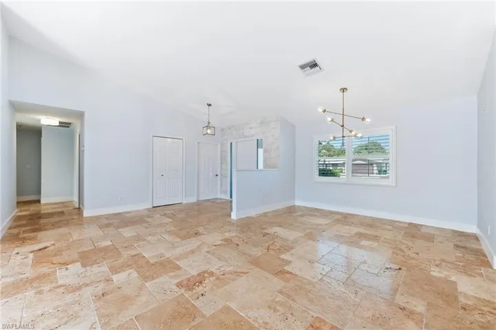 Empty room featuring an inviting chandelier, vaulted ceiling, stone tile floors, and visible vents