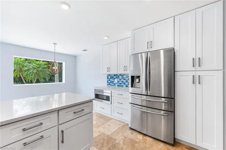 Kitchen featuring light stone counters, stainless steel fridge with ice dispenser, decorative backsplash, white cabinets, and decorative light fixtures