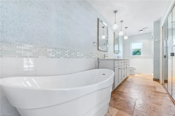 Full bath with toilet, stone tile floors, tile walls, a soaking tub, and vanity